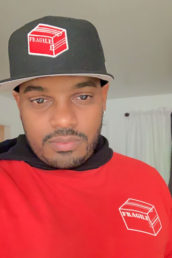 Chris, owner of Fragile Service Care, in a red Fragile shirt and Fragile hat