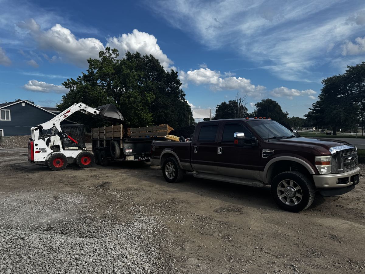 Skid steer loading a dump trailer hitched to the crew's pickup truck