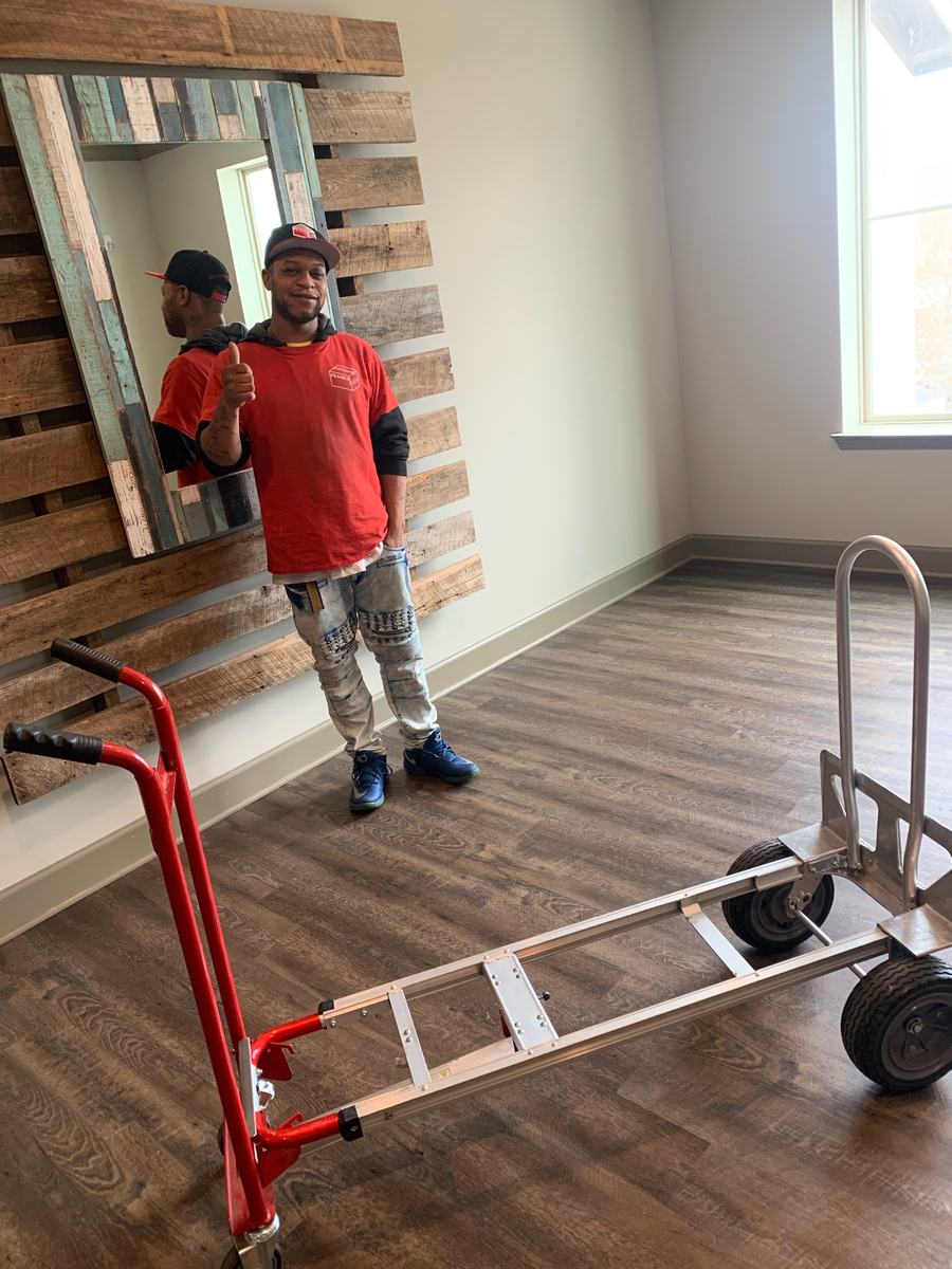 Crew member in a red Fragile shirt giving a thumbs up in an emptied room next to a hand truck