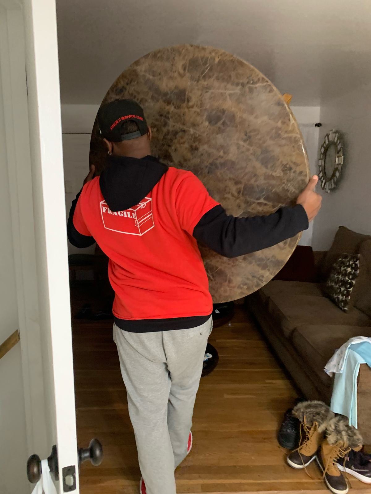 Fragile Service Care crew member in a red FRAGILE hoodie carefully carrying a round marble tabletop through a living room