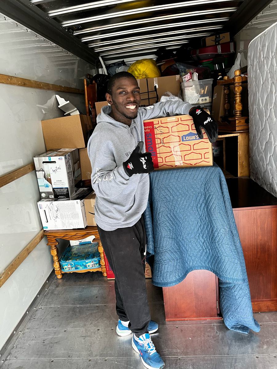 Crew member giving a thumbs up inside a rental truck loaded tight with boxes and furniture under moving blankets